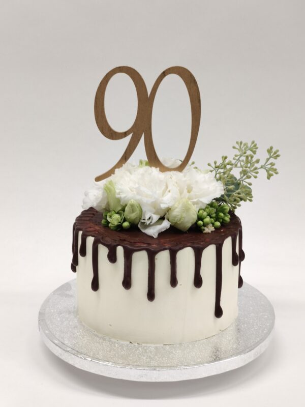 Weiße Geburtstagstorte aus Buttercreme mit dunklem Schokoladendrip, frischen Blumen und "90" Holztopper